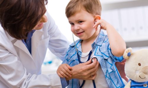 Senior female doctor examining happy child, smiling.